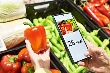 Checking calories on red bell pepper vegetable in store with smartphone