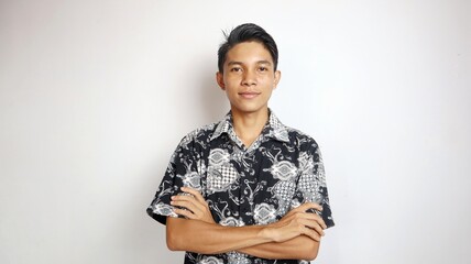 smiling young handsome Asian man wearing batik shirt posing with crossed arms