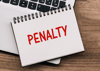 A notepad with the word penalty written on it placed next to a laptop on a desk.