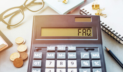 Calculator Displaying FAQ With Coins, Glasses, and Notepad on Desk