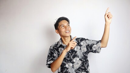 Happy young handsome Asian man wearing batik shirt posing pointing at the top of the open copy space