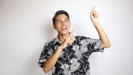 Happy young handsome Asian man wearing batik shirt posing pointing at the top of the open copy space