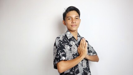 Excited handsome young Asian man dressed in batik with greeting gesture