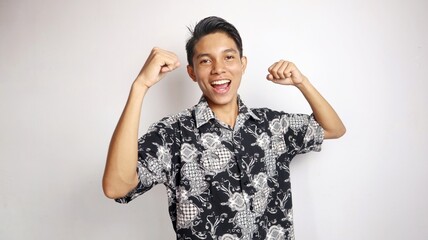happy young handsome asian man wearing batik shirt posing raising hands excitedly, enthusiastically, winning