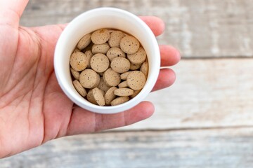 Top view of a person holding a white bowl filled with brewer's yeast on a wooden background