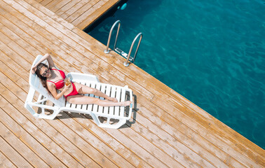Happy slender girl lying with a cocktail on a poolside lounger. Concept of summer rest and vacation. Background with copy space.