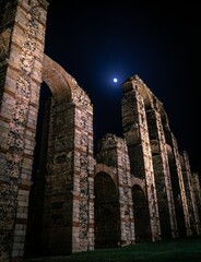 Vertical shot of the Acueducto de los Milagros Roman aqueduct under a shining moon in Merida, Spain - obrazy, fototapety, plakaty