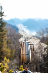 Vertical shot of a manual coffee maker on the edge of a cliff with hot steam