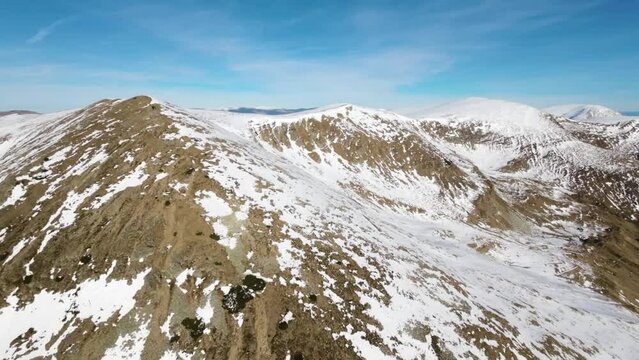 Drone view of mountains covered in the snow under the sunlight and a blue sky in 4K