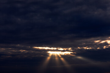 Sunset in the sky with rays of light through the clouds. Dark cloudscape with light beam