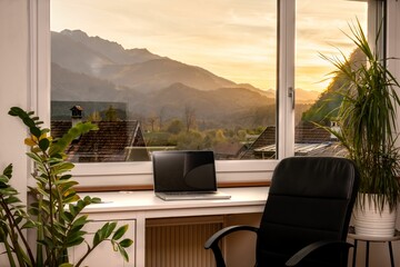 Laptop on the windowsill with a beautiful view of mountains at sunset. Home office, remote job.