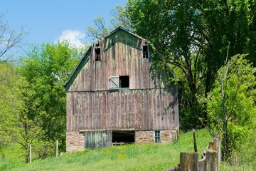 Old wooden barn with grass and green trees around in the rural Wisconsin on a sunny day - obrazy, fototapety, plakaty