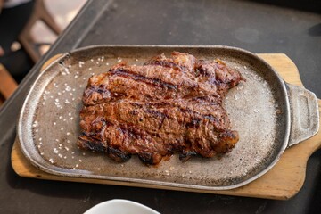 Flat lay closeup of a delicious steak with coarse salt sprinkled on top of an iron platter