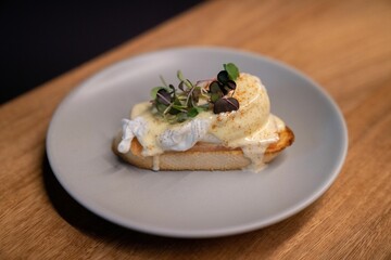 Piece of eggs benedict with delicious garnish on wooden table at restaurant for brunch
