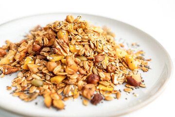 A bowl of granola with nuts and seeds on a white plate. The granola is a mix of different types of grains and nuts, and it looks like a healthy snack.