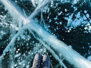 Fragile thin brittle ice underfoot. Female feet on ice. Woman wearing winter shoes - obrazy, fototapety, plakaty