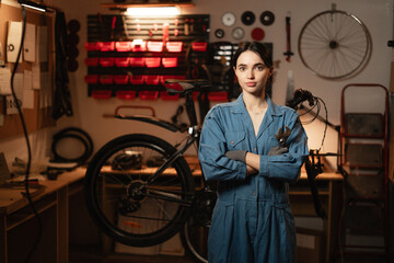 Bicycle repairing and diy concept. Portrait of young woman standing with a bicycle and tools in the workshop or authentic garage at home.