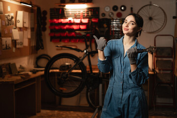 Portrait of a beautiful repairwoman in workwear at the bicycle workshop pointing with finger on space for text