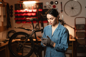 Mechanic reading a message on smartphone in bicycle workshop, she is repairing or servicing in a garage