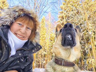 Adult girl or mature lady with shepherd dog taking selfies in winter nature landscape in a forest....