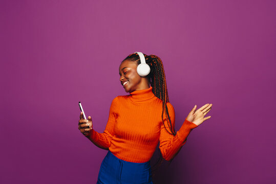 Happy girl dancing and holding a smartphone with vibrant purple background