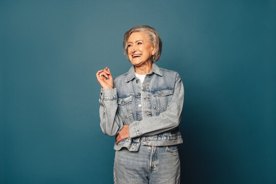 Confident mature woman in casual denim outfit smiling and standing on blue background