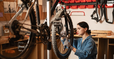 Young female mechanic fixing wheel on a bicycle during a repairman in workshop or garage. bike repair