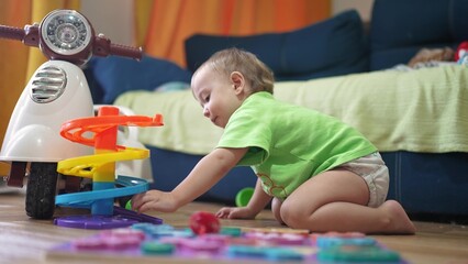 baby child plays with a toy slide and rolls a ball. happy family kid dream concept. baby play indoors with toys develops fine motor skills lifestyle. baby plays with toys in kindergarten