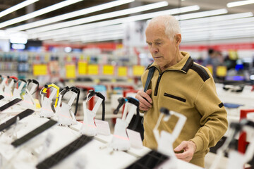 Elderly man examines smart watch in showroom of electronics store - obrazy, fototapety, plakaty
