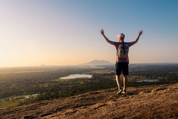 Rear view of man with backpack enjoying sunset. Happy solo traveler with raised arms in Sri Lanka.. - 786132952