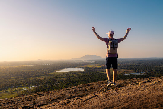 Rear view of man with backpack enjoying sunset. Happy solo traveler with raised arms in Sri Lanka..