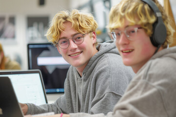 Two smiling young men in glasses and working on a laptop in an office.