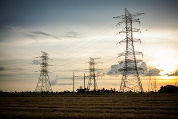 High-voltage power lines at sunset. High voltage electric transmission tower at paddy field.