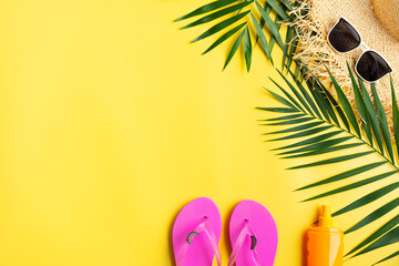 Vacation travel planning simple theme of straw hat sunglasses flip flops and palm leaves on uniform yellow background flat lay with copy-space