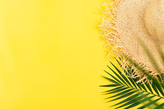 Vacation travel planning simple theme of straw hat and palm leaves on uniform yellow background flat lay with copy-space