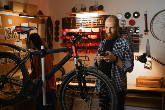 Mechanic in a bicycle repair workshop using smartphone reading a message or searching information online about bike.