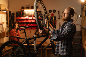 male worker holding and repairing bicycle wheel while standing in bicycle workshop or authentic garage.