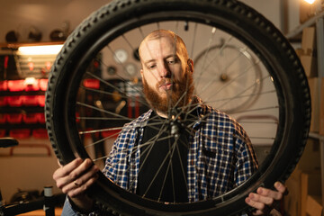 Bearded man standing alone in his workshop or garage and repairing a bicycle wheel.