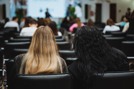 Two women sitting in a lecture hall watching a presentation