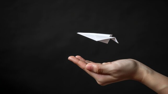 The image shows a hand throwing a white paper plane against a black background.