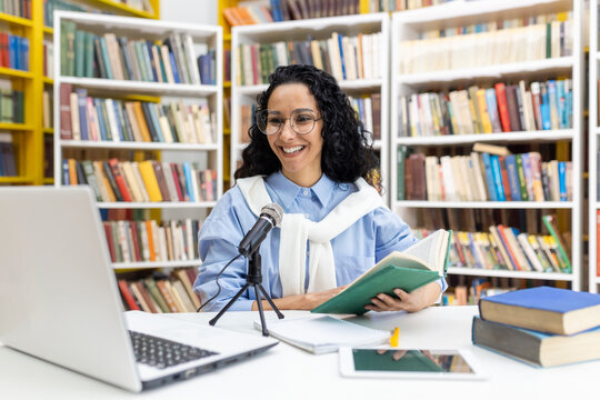 In a vibrant library, a cheerful librarian with curly hair speaks into a microphone while holding a book, surrounded by shelves filled with books.