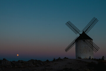 A windmill is standing in a field at night, the sky is dark and the moon is visible in the distance