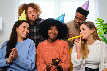 Multiracial happy friends celebrating a birthday party with party horns and hats.