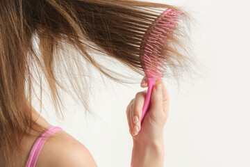 Hair care. Close up view of brunette woman combing her dry damaged hair with plastic detangling hair brush.