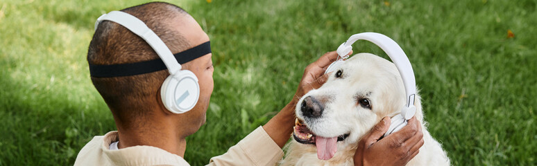 A disabled African American man with myasthenia gravis syndrome holding a Labrador dog wearing headphones, showcasing diversity and inclusion.