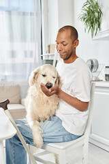 A disabled African American man sitting in a chair, peacefully cradling a Labrador dog in his arms.