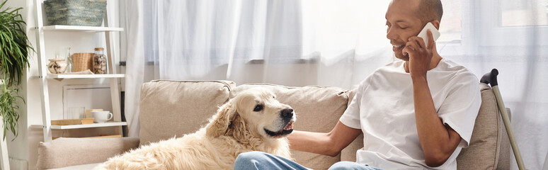 A man with myasthenia gravis sits on a couch talking on a cell phone next to his loyal Labrador dog.
