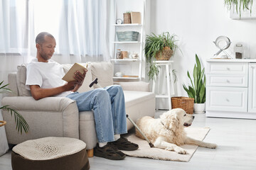 An African American man with myasthenia gravis is seated on a couch, reading a book, accompanied by...