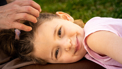 Maternal bonding: Caucasian little girl smiles on her mother's lap in sunny park