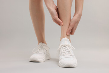 Woman suffering from leg pain on grey background, closeup